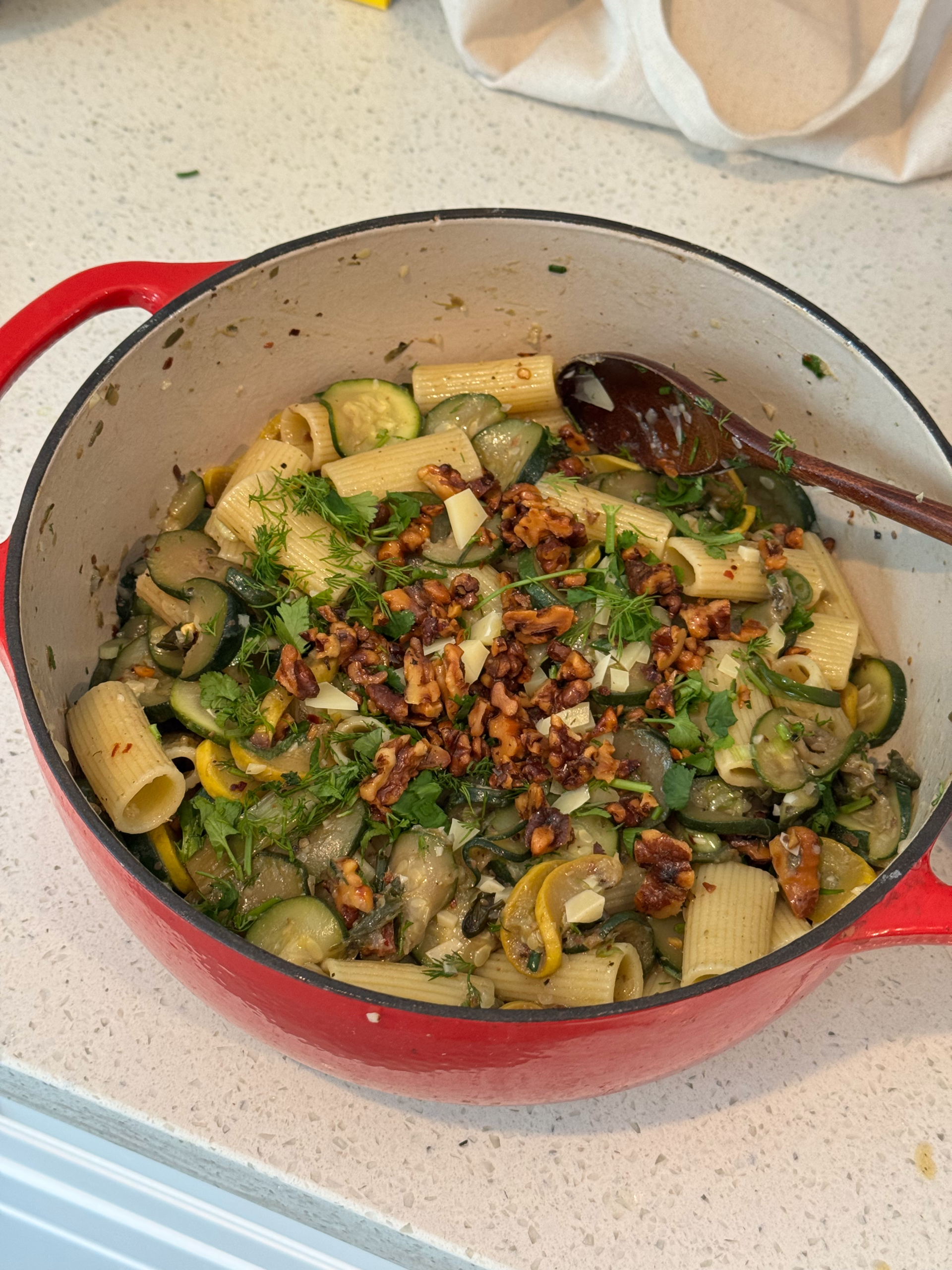 a pot of pasta with walnuts, squash, herbs, in a red dish sitting on a counter